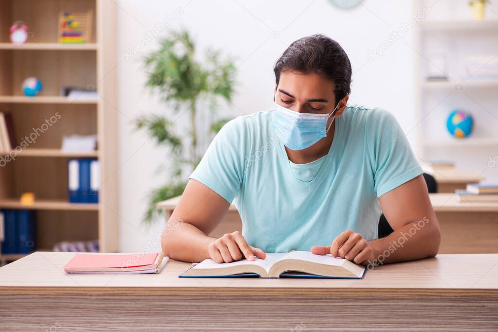 Young male student sitting in the classroom wearing mask