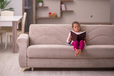 Evde kitap okuyan küçük bir kız.