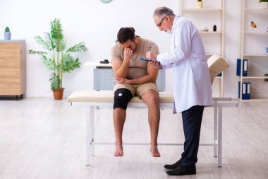 Deneyimli doktor travmatolog genç erkek hastayı muayene ediyor.