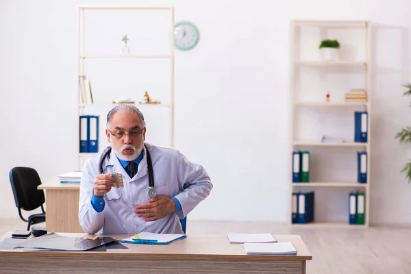 Old male doctor writing prescription in the clinic