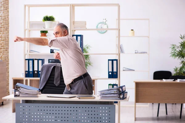 Velho funcionário do sexo masculino fazendo exercícios físicos no local de trabalho — Fotografia de Stock