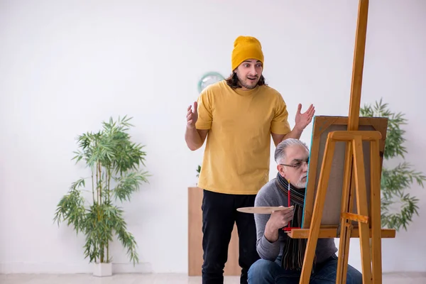 Old man taking lesson from young painter