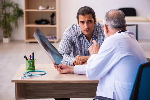 Jovem paciente masculino visitando idoso médico masculino — Fotografia de Stock