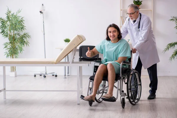 Paciente masculino joven en silla de ruedas y traumatólogo médico experimentado —  Fotos de Stock