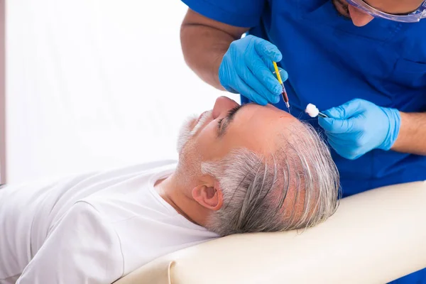 Старик посещает молодого врача-мужчину в конусе для трансплантации волос — стоковое фото