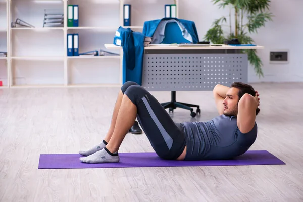 Young handsome employee doing sport exercises in the office