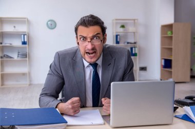 Ofisteki aşırı işten memnun olmayan genç bir erkek işçi.