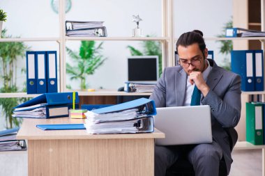 Genç bir erkek çalışan ve ofiste çok fazla iş var.