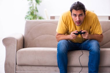 Genç adam evde joystick oynuyor.