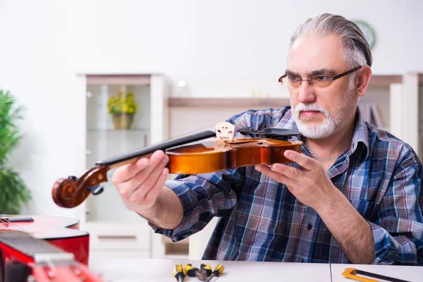 Senior mannelijke reparateur die thuis muziekinstrumenten repareert — Stockfoto
