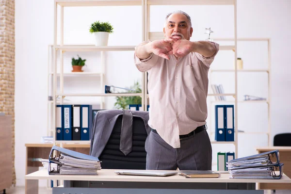 Viejo empleado haciendo ejercicios físicos en el lugar de trabajo —  Fotos de Stock