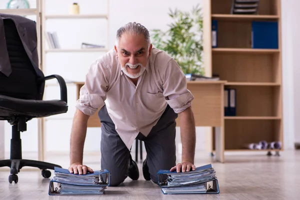 Velho funcionário do sexo masculino fazendo exercícios físicos no local de trabalho — Fotografia de Stock