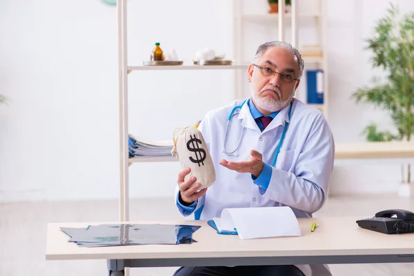 Velho médico masculino segurando saco de dinheiro no hospital — Fotografia de Stock