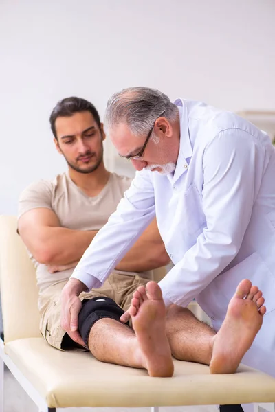 Médico traumatólogo experimentado examinando paciente varón joven — Foto de Stock