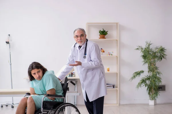 Jovem paciente do sexo masculino em cadeira de rodas e médico traumatologista experiente — Fotografia de Stock