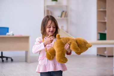 Küçük kız elinde oyuncak ayı klinikte doktoru bekliyor.