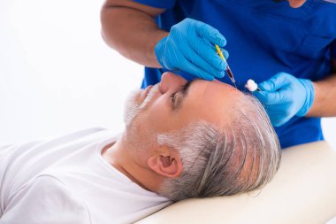 Yaşlı adam saç nakli için genç erkek doktoru ziyaret ediyor.