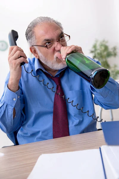 Oude mannelijke werknemer drinkt alcohol op kantoor — Stockfoto