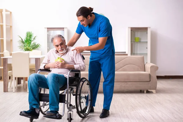 Oude man in rolstoel en jonge slechte verzorger binnen — Stockfoto