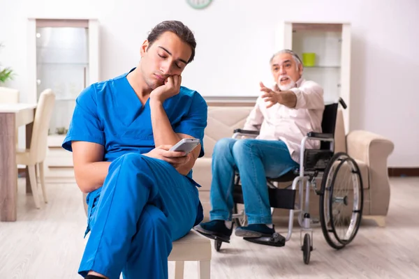 Oude man in rolstoel en jonge slechte verzorger binnen — Stockfoto