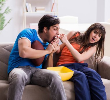 Adam karısıyla Amerikan futbolu seyrediyor.