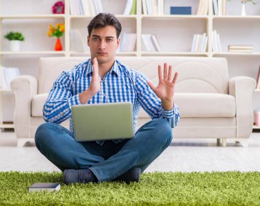 Genç yakışıklı adam evde yerde oturuyor.