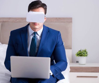 Yatak odasında sanal gerçeklik kulaklığı takan bir iş adamı.