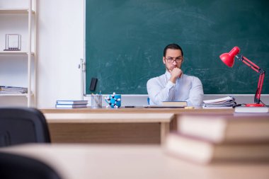 Genç erkek öğretmen yeşil panonun önünde.