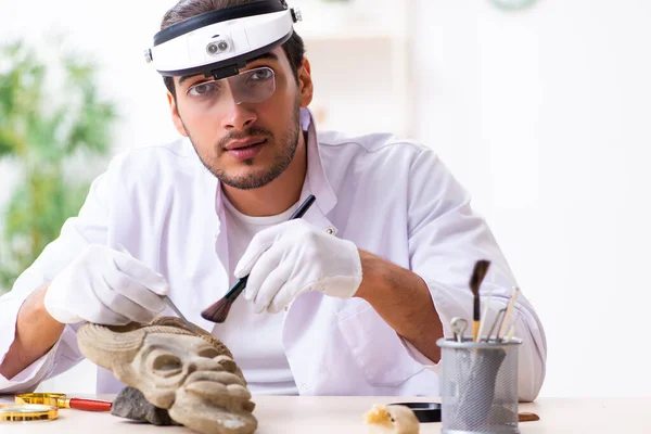 Jonge mannelijke archeoloog bestudeert het oude Afrikaanse steenmasker — Stockfoto