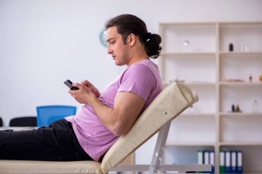 Akıllı telefonu olan genç bir erkek hasta doktor bekliyor.