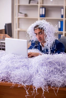 Genç bir erkek çalışan ve ofiste bir sürü kesik kağıt var.