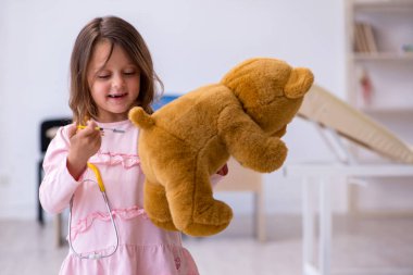 Küçük kız elinde oyuncak ayı klinikte doktoru bekliyor.
