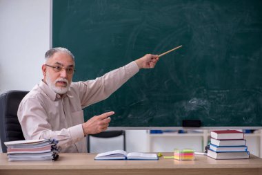 Sınıfta oturan yaşlı erkek öğretmen.
