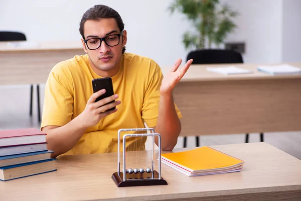 Joven estudiante masculino sosteniendo el teléfono móvil durante la preparación del examen —  Fotos de Stock