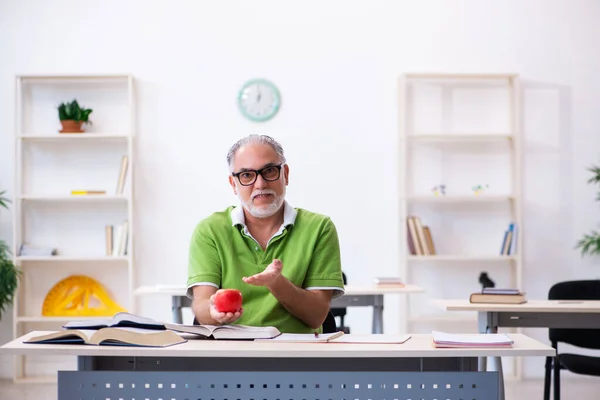 Old male student eating apple during exam preparation — Stock Photo, Image