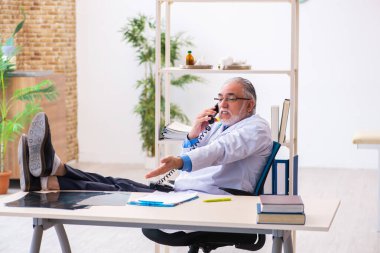 Yaşlı erkek doktor klinikte telefonla konuşuyor.