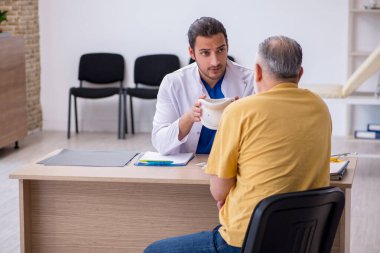 Yaşlı boynu yaralı bir adam genç erkek doktoru ziyaret ediyor.