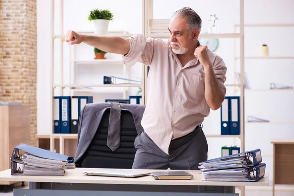 Old male employee doing physical exercises at workplace — Stock Photo, Image