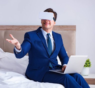 Yatak odasında sanal gerçeklik kulaklığı takan bir iş adamı.