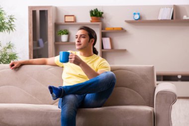 Genç bir öğrenci evde kahve içiyor.