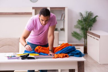 Genç erkek terzi salgın sırasında evde maske dikiyor.