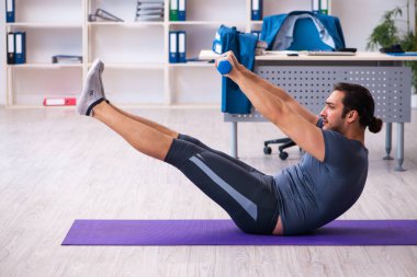 Genç yakışıklı çalışan ofiste spor egzersizleri yapıyor.