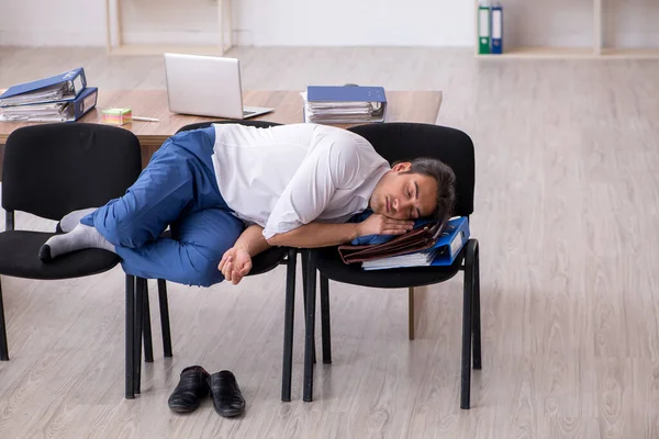 Młody pracownik śpi w biurze na krzesłach — Zdjęcie stockowe