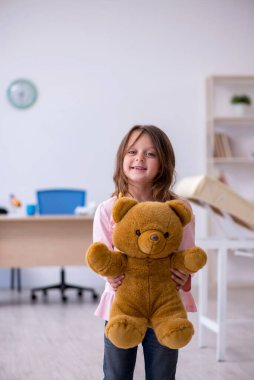 Küçük kız elinde oyuncak ayı klinikte doktoru bekliyor.