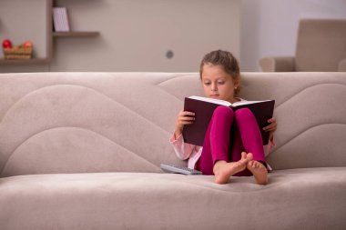 Evde kitap okuyan küçük bir kız.