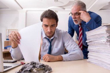 Genç erkek çalışan ve yaşlı patron iş yerinde kağıtları yakıyor.
