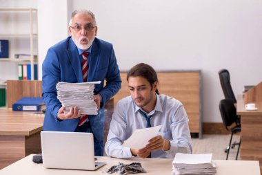 Genç erkek çalışan ve yaşlı patron iş yerinde kağıtları yakıyor.