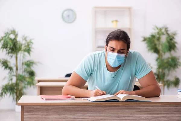 Ung manlig student sitter i klassrummet bär mask — Stockfoto