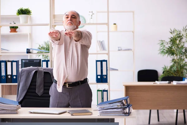 Starý muž zaměstnanec dělá fyzická cvičení na pracovišti — Stock fotografie