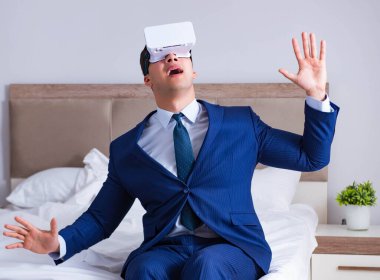 Yatak odasında sanal gerçeklik kulaklığı takan bir iş adamı.